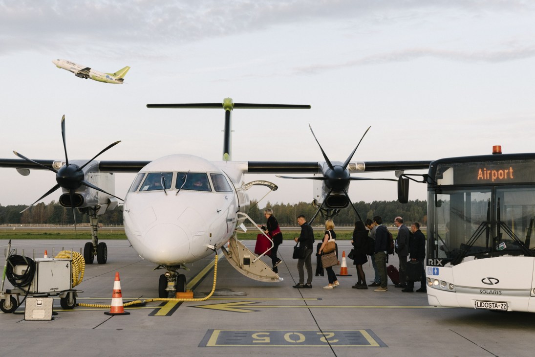 AirBaltic Bombardier Dash 8-Q400 aircraft on airport tarmac with passengers boarding via stairs and airport bus nearby.