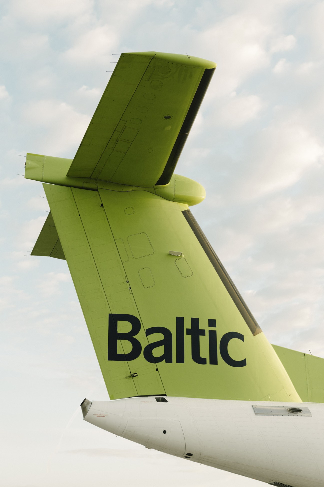 Close-up of AirBaltic Bombardier Dash 8-Q400 aircraft tail with distinctive lime-green livery and black 'Baltic' text against cloudy sky