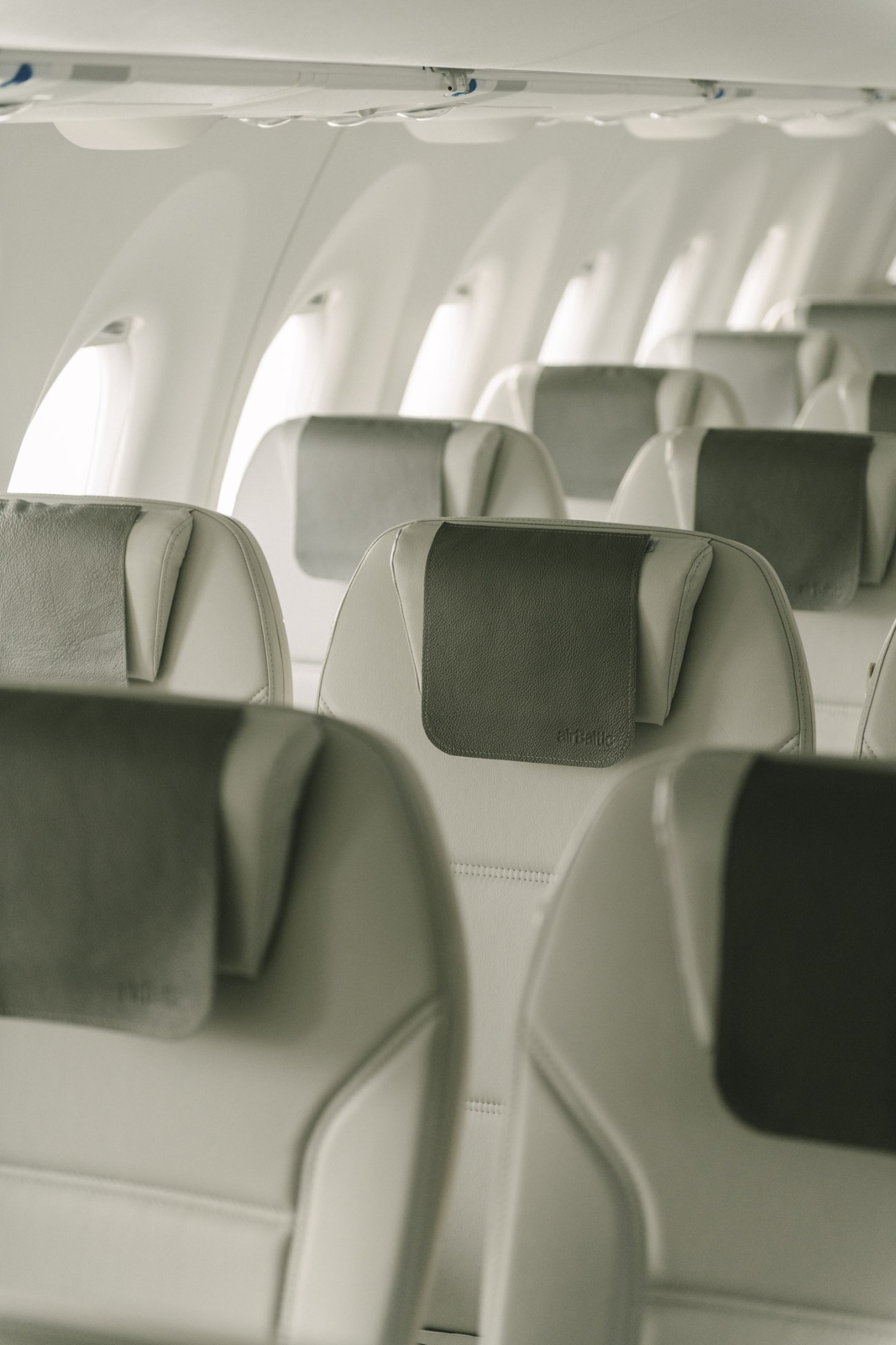 Interior of an Airbus A220 passenger cabin with pale grey and white modern seating and windows.