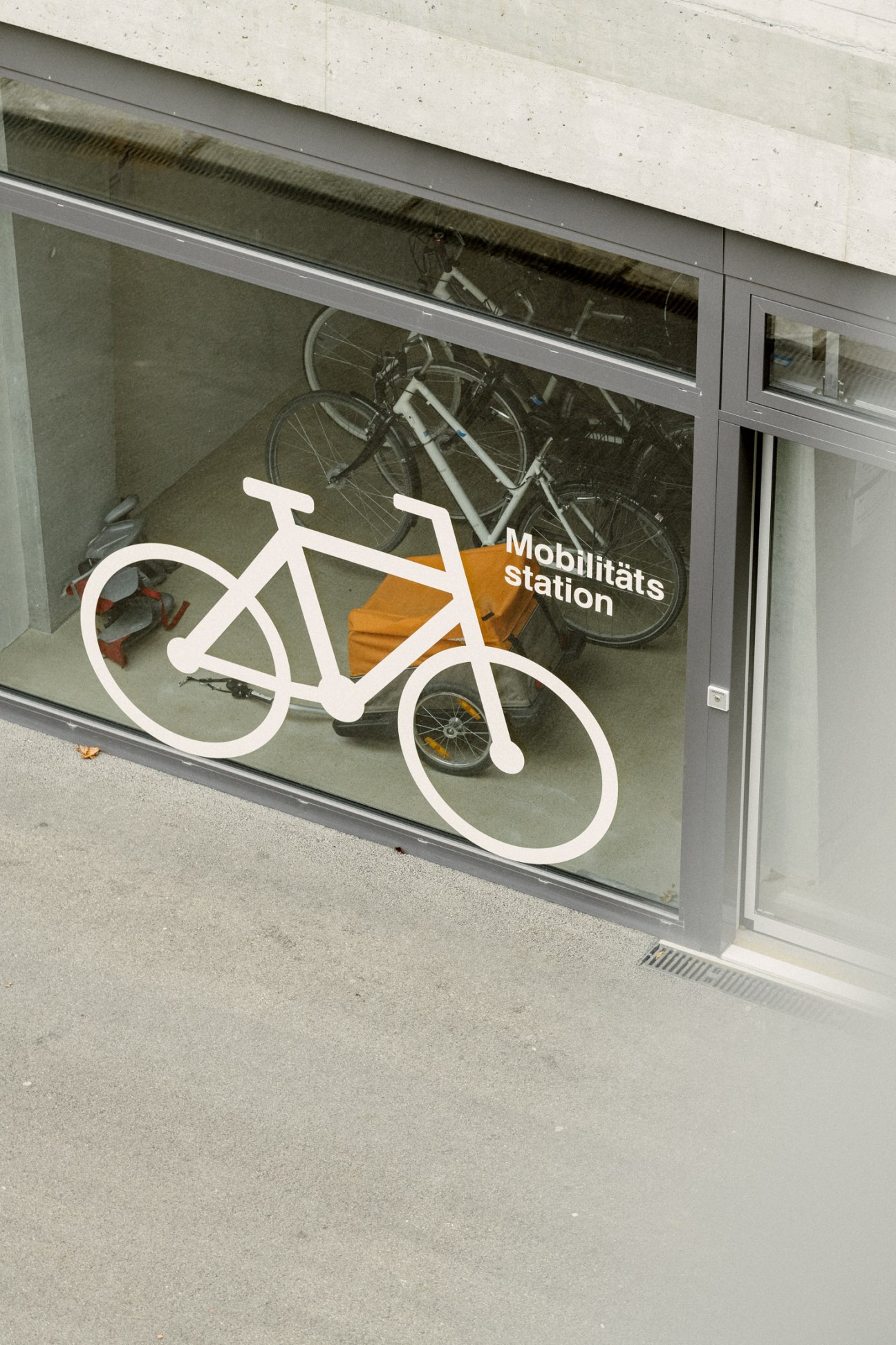 Bicycle garage window with white bike outline graphic and 'Mobilitäts station' text, showing parked bicycles inside.