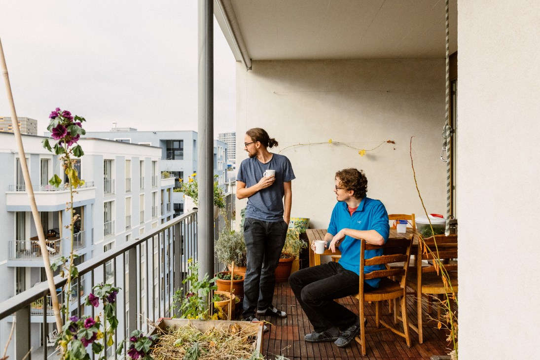 Samuel Müller with a flatmate on a rooftop terrace with flowering plants and residential buildings in the background.