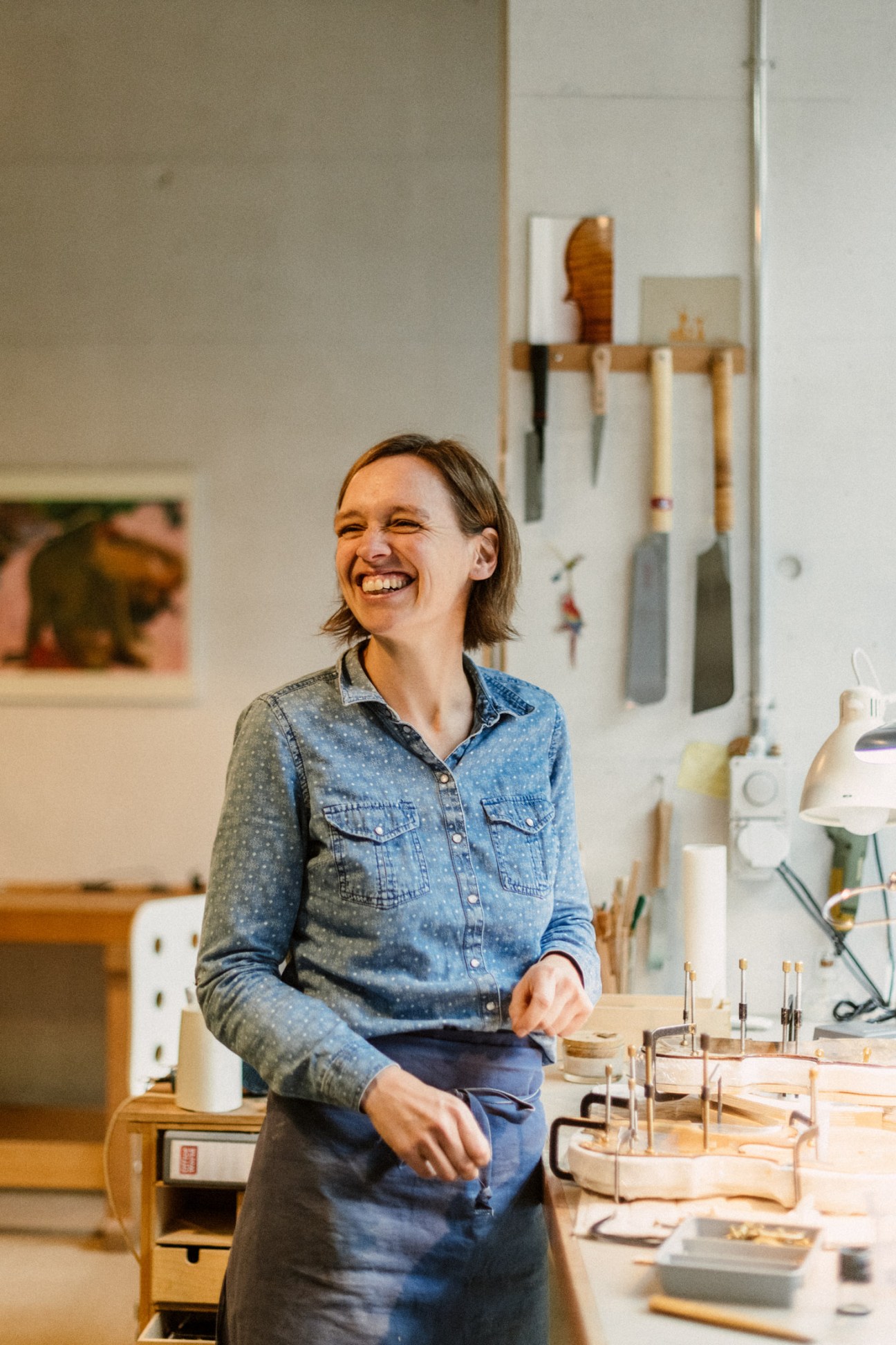 Violin-maker Julia Van Der Waerden smiling in her workshop surrounded by instruments and tools.