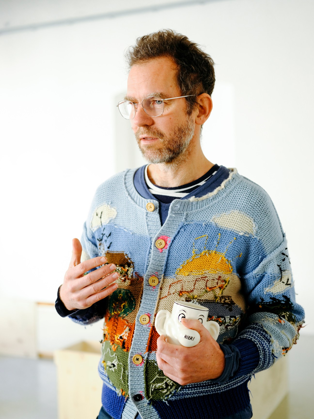 Tobias Urban of Gelitin holds a ceramic vessel while wearing a patterned cardigan.