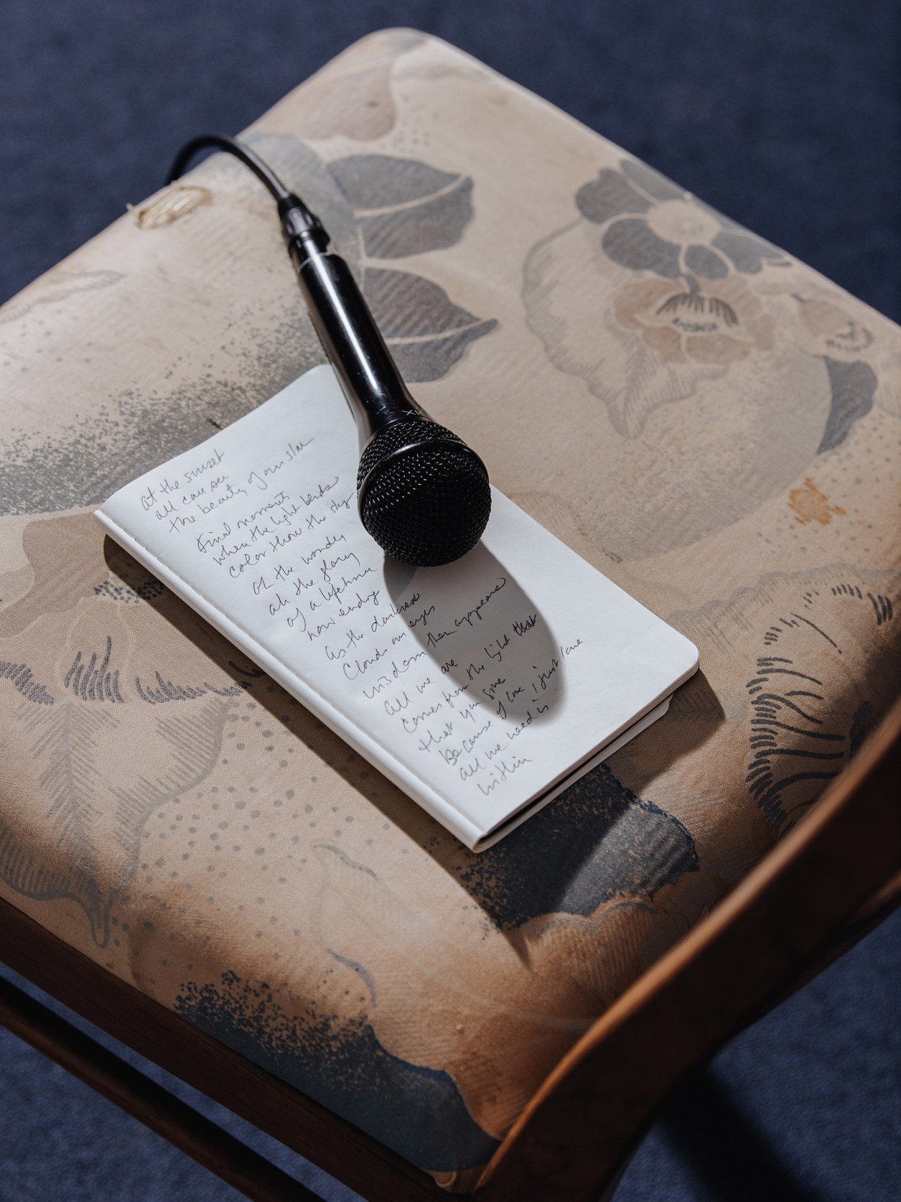 A microphone rests on a handwritten notebook page with lyrics or notes, placed on African-patterned fabric.