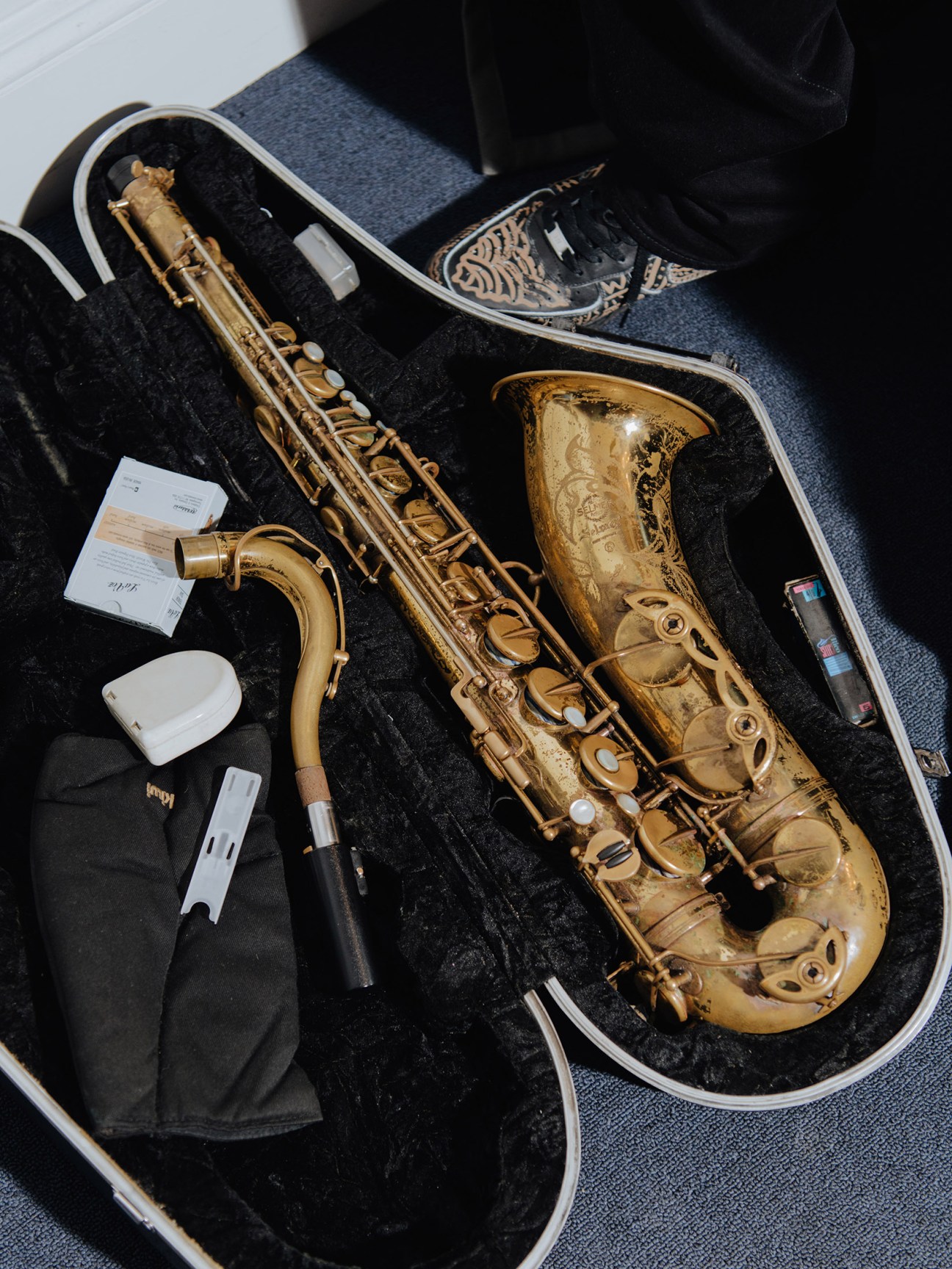 A Selmer Mark VI saxophone in an open case with maintenance accessories and a patterned shoe visible above.