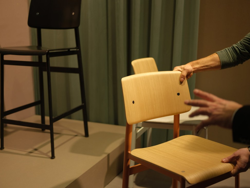 Hands examining a light wood chair with a curved backrest at a furniture fair display.