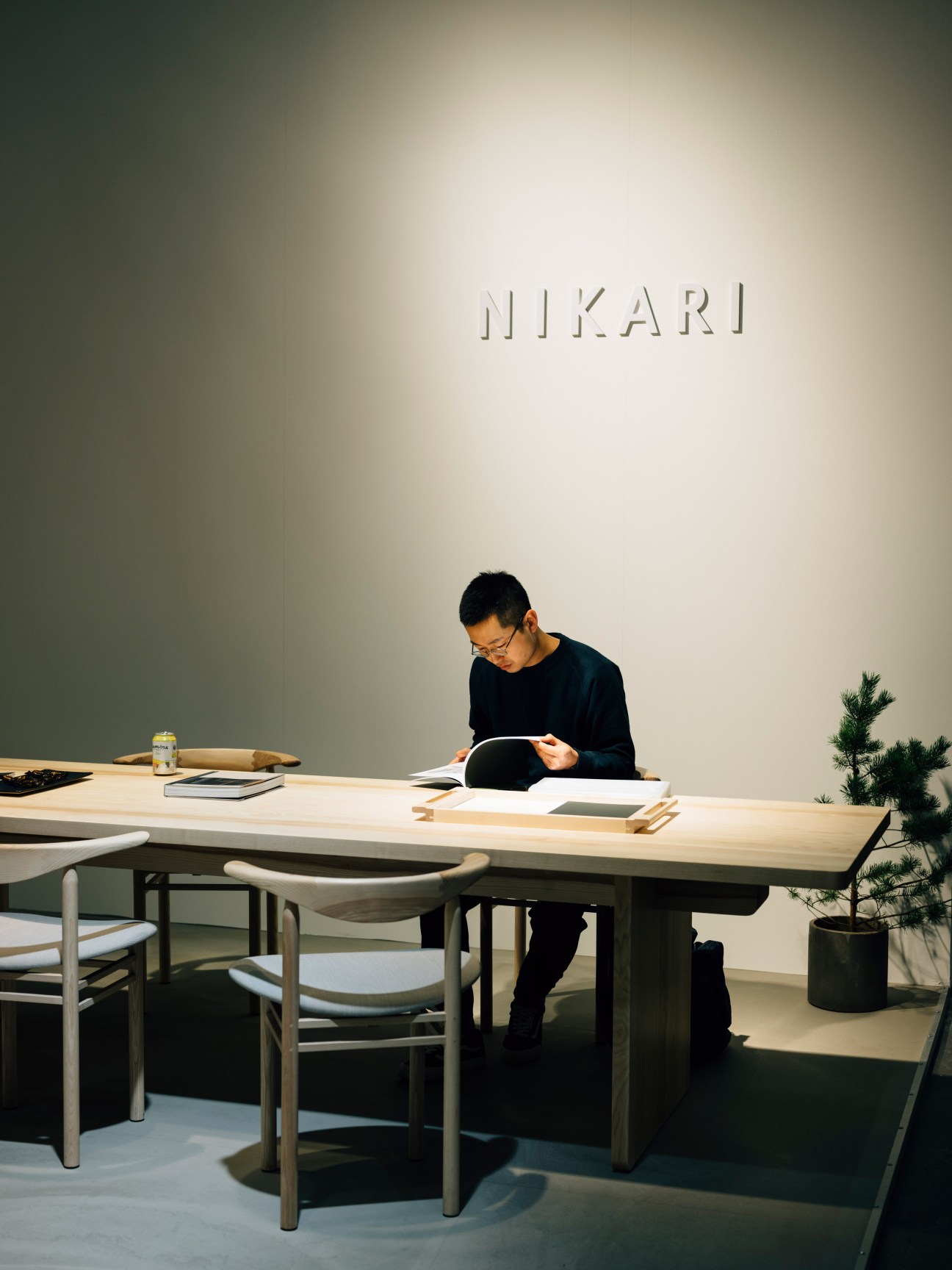 Person reading at wooden table beneath Nikari signage in minimalist interior.