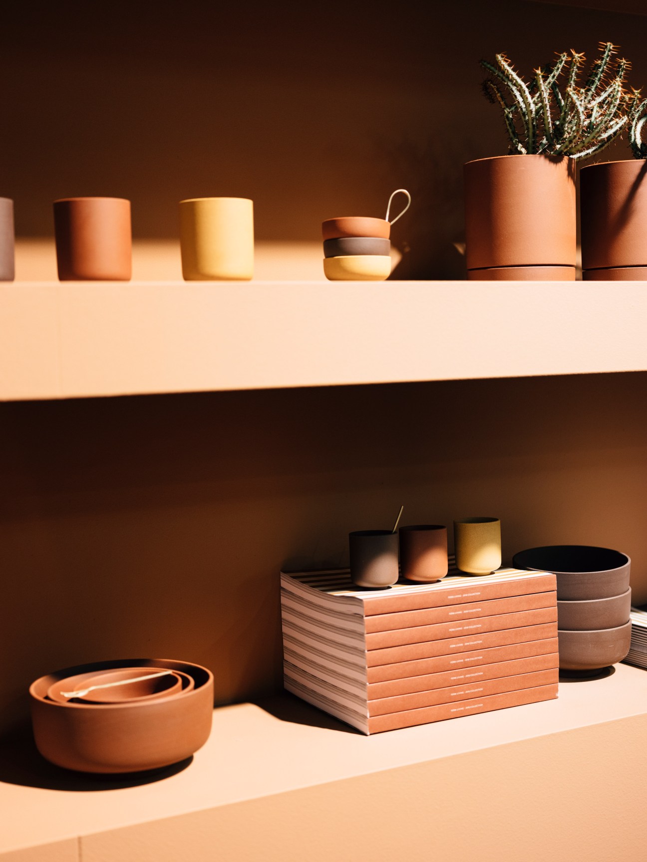 Terracotta and neutral-toned ceramic vessels and planters displayed on white shelving with earthy colour palette.