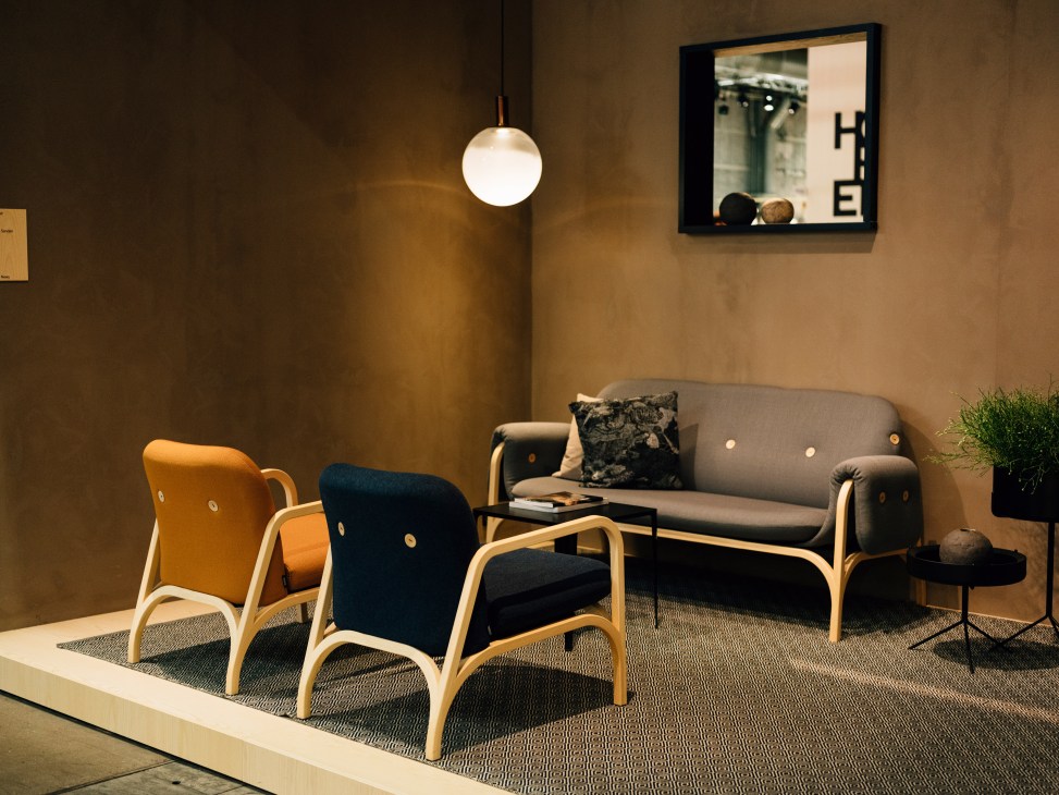Scandinavian furniture showroom display with orange and navy upholstered chairs, gray sofa, pendant light, and styled accessories.