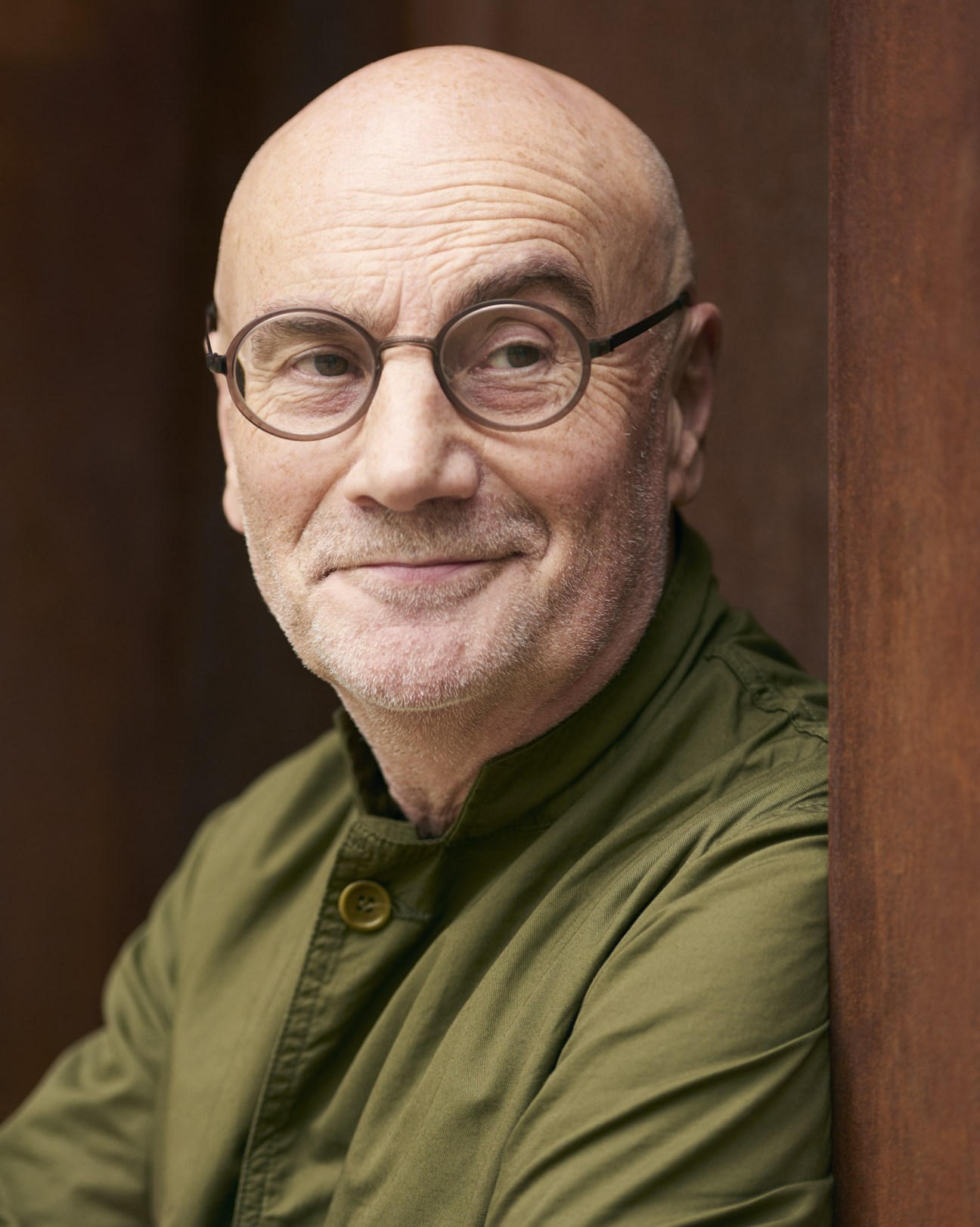 Portrait of Adrian Shaughnessy, a bald man with glasses wearing a green jacket.