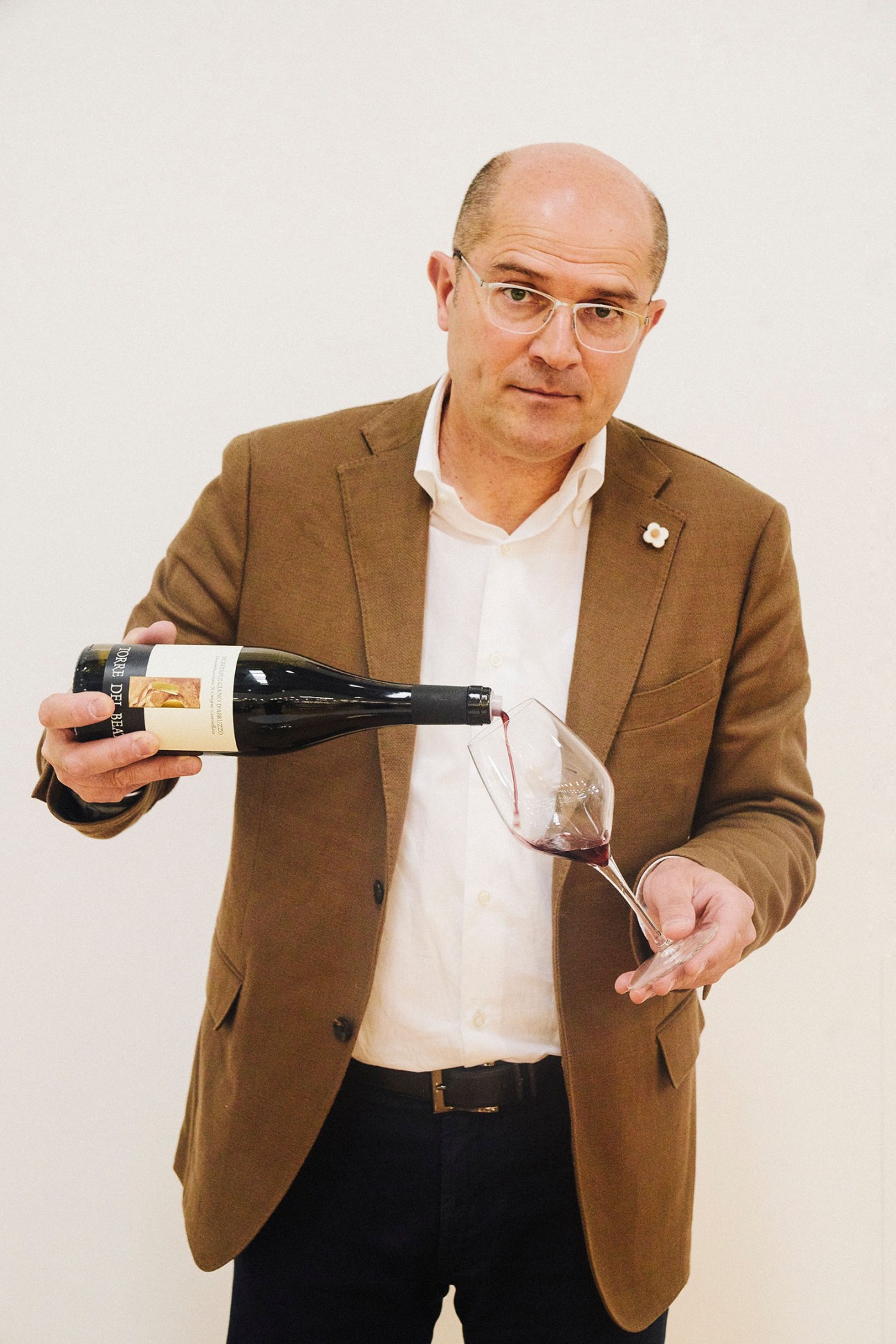 Fausto Albanesi of Torre Dei Beati holds a wine bottle and glass against a white background.