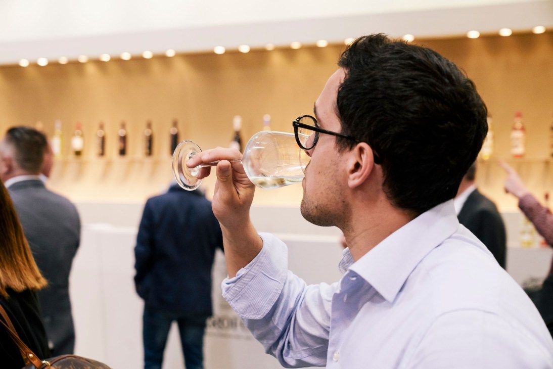 A man in glasses and light blue shirt tastes white wine from a glass at Vinitaly wine fair in Verona.