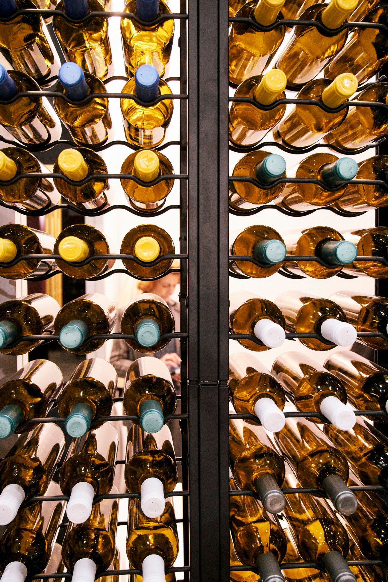 Wine bottles with various colored caps displayed on a black metal rack at Vinitaly.