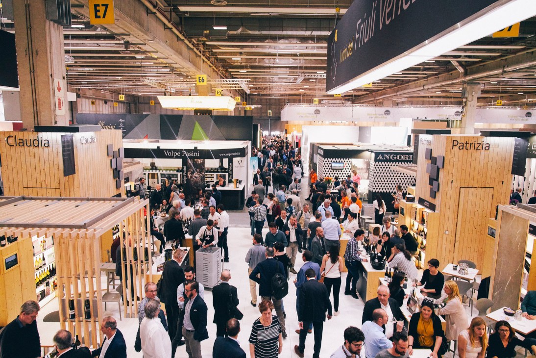 Overhead view of crowded Vinitaly wine exhibition floor with wooden booths and visitors.