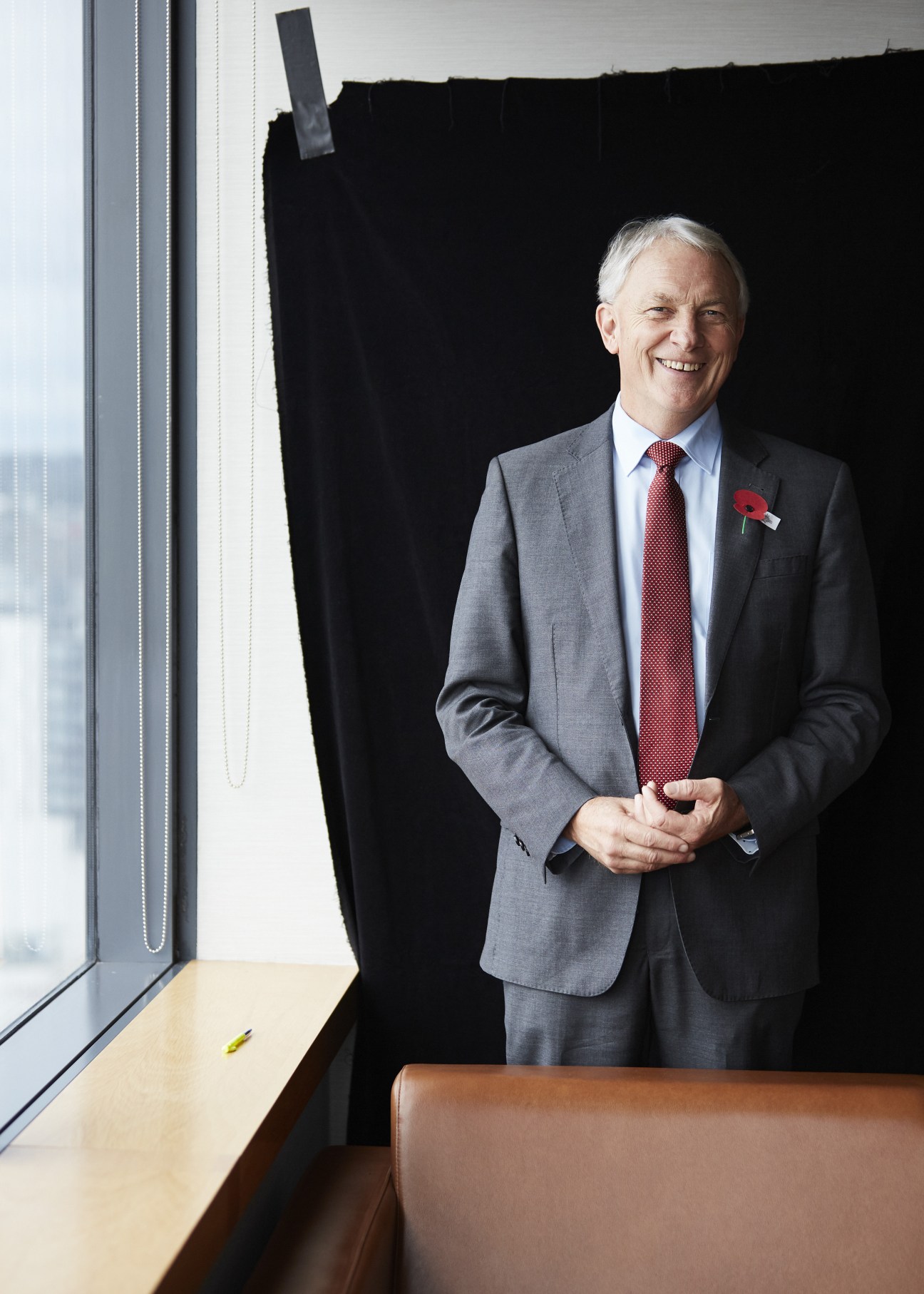 Phil Goff, Auckland mayor, stands in an office wearing a grey suit and burgundy tie with a poppy pin.