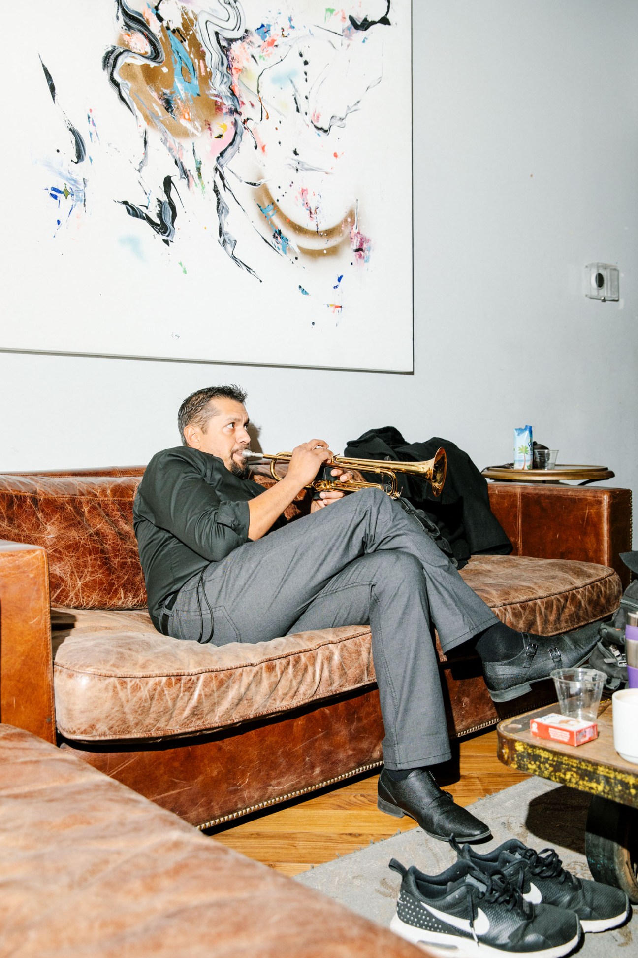 Jacob Valenzuela plays trumpet while sitting on a brown leather couch in a greenroom.