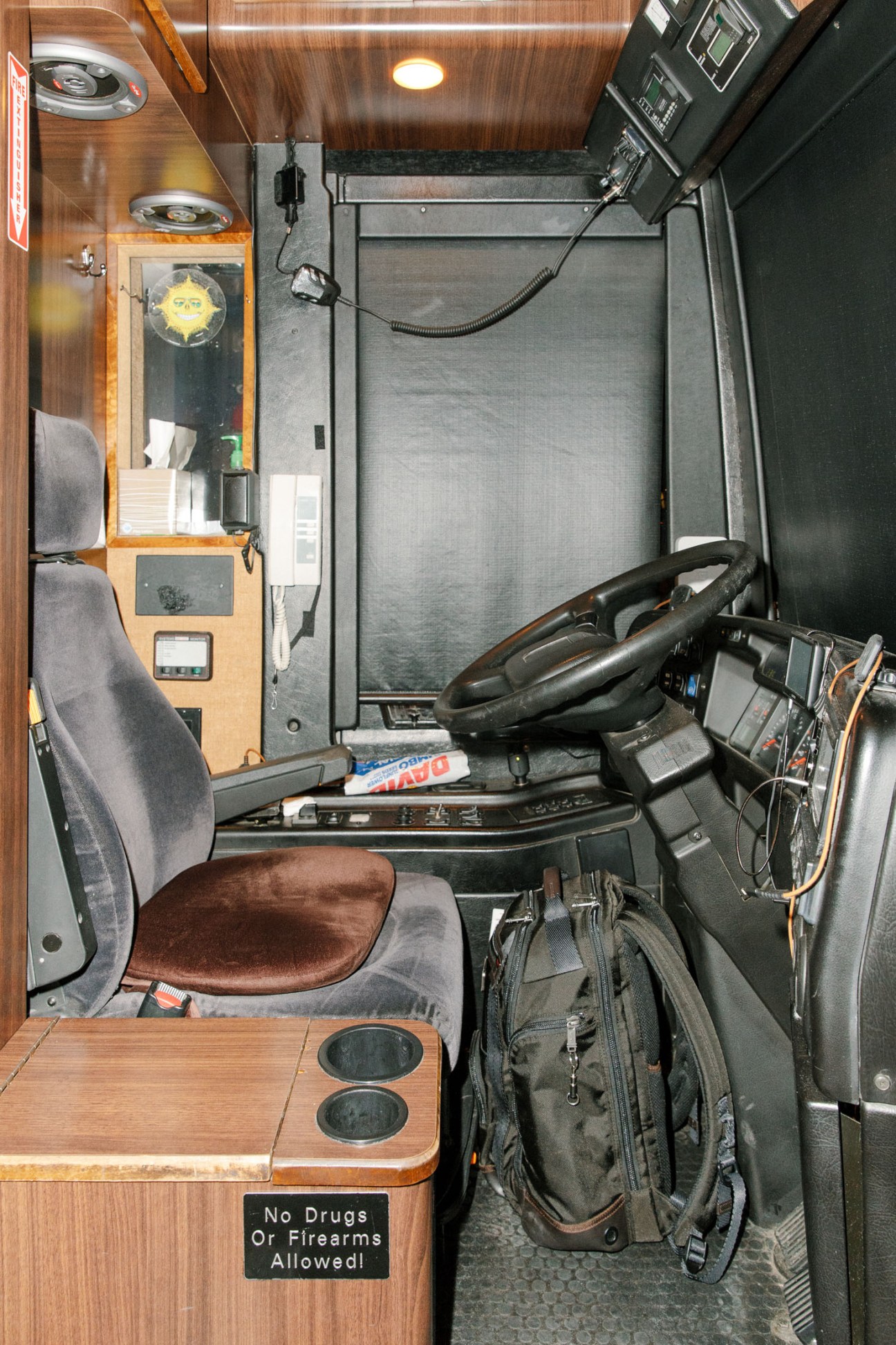 Interior view of a tour bus driver's seat with steering wheel, wooden dashboard, and control panels.