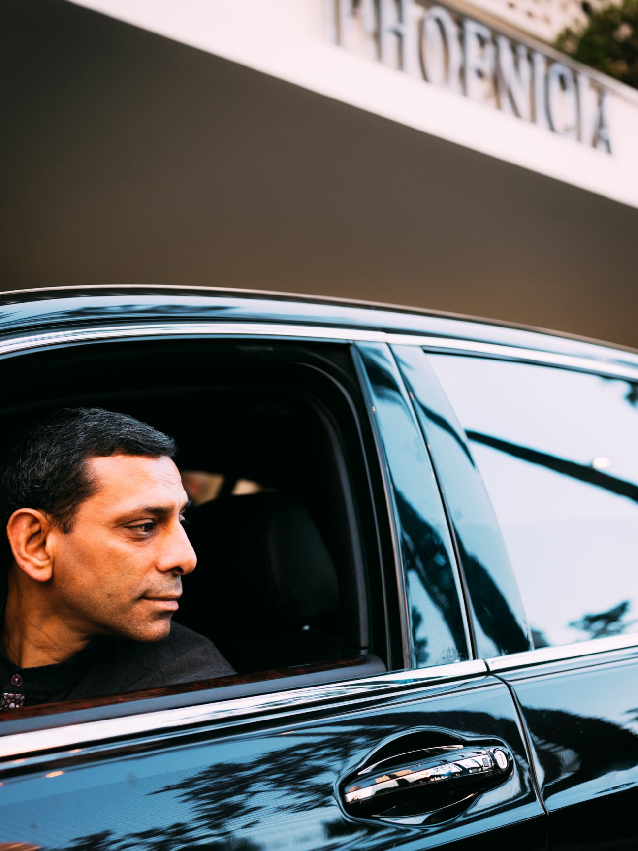 A valet driver in dark clothing looks out from the open window of a dark-colored car.