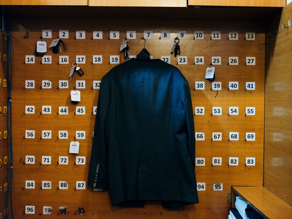 A dark blue jacket hangs on a wooden key board with numbered hooks in a valet parking stand.