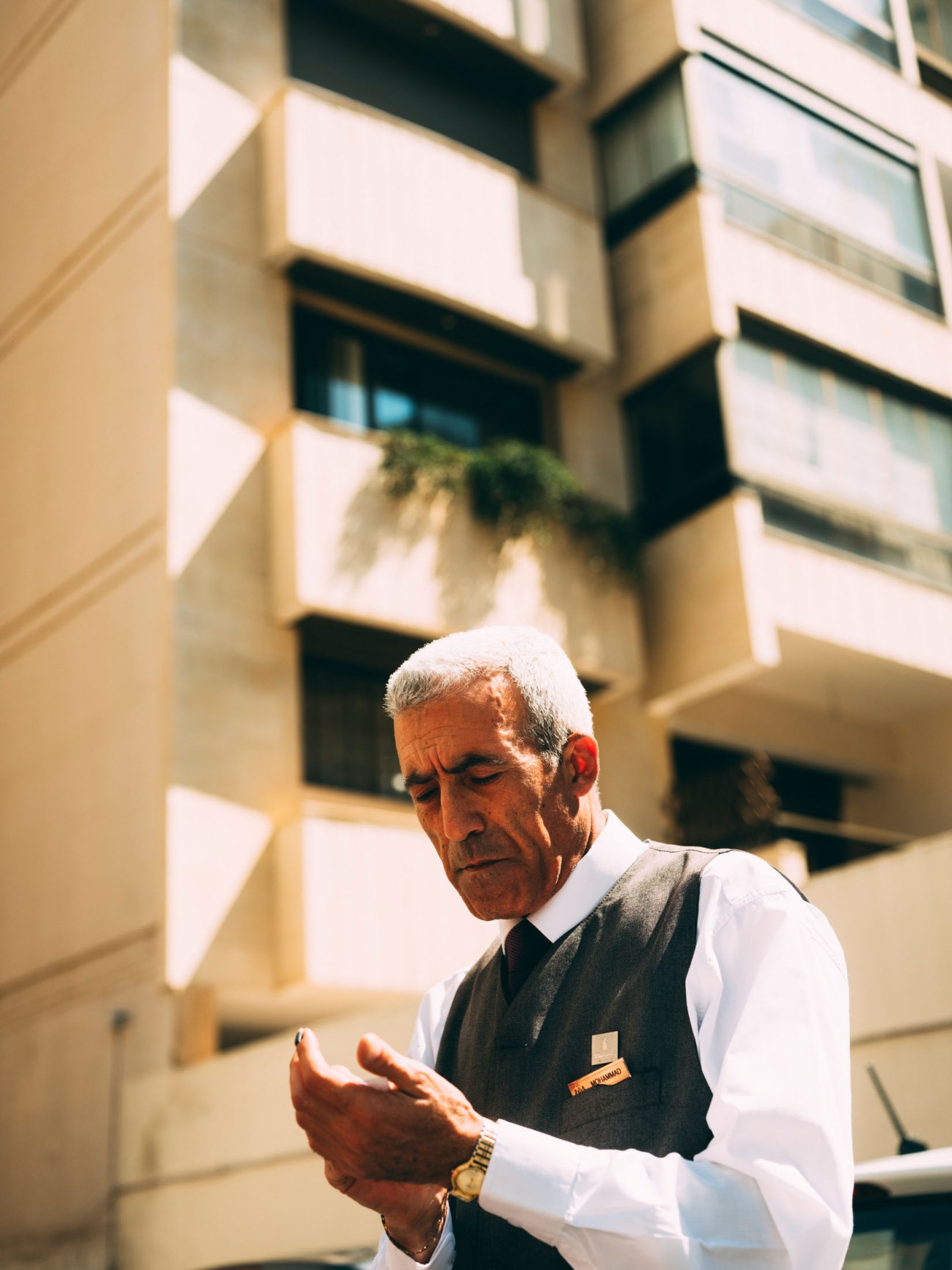 Beirut valet in white shirt and grey waistcoat standing against apartment building.