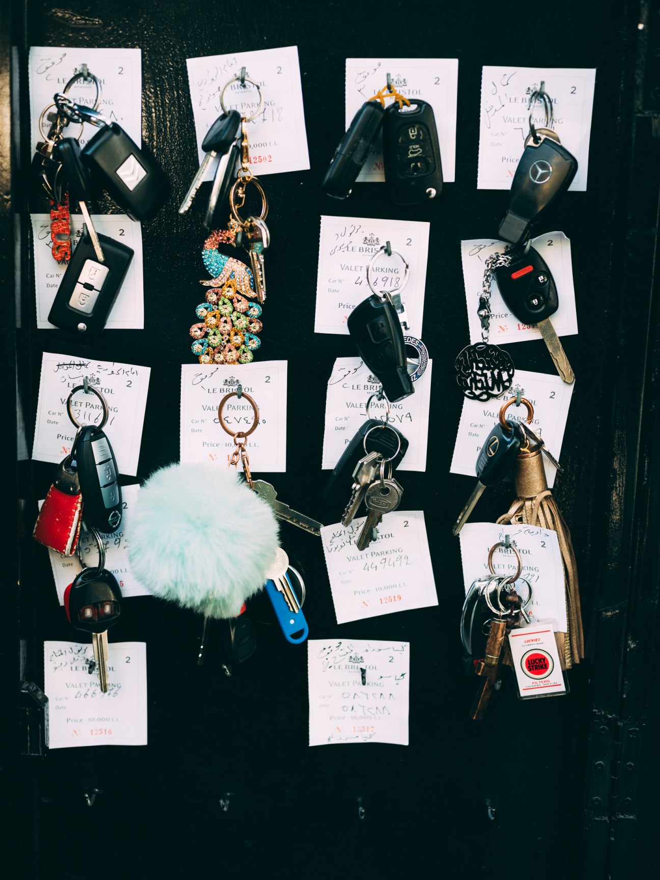 Multiple car keys with decorative keychains and handwritten valet parking tickets arranged on a dark surface.