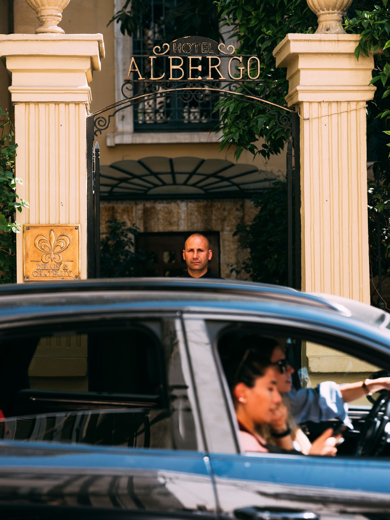 A valet attendant stands in the ornate entrance of Hotel Albergo in Beirut, watching as a car approaches with a driver visible through the windshield.