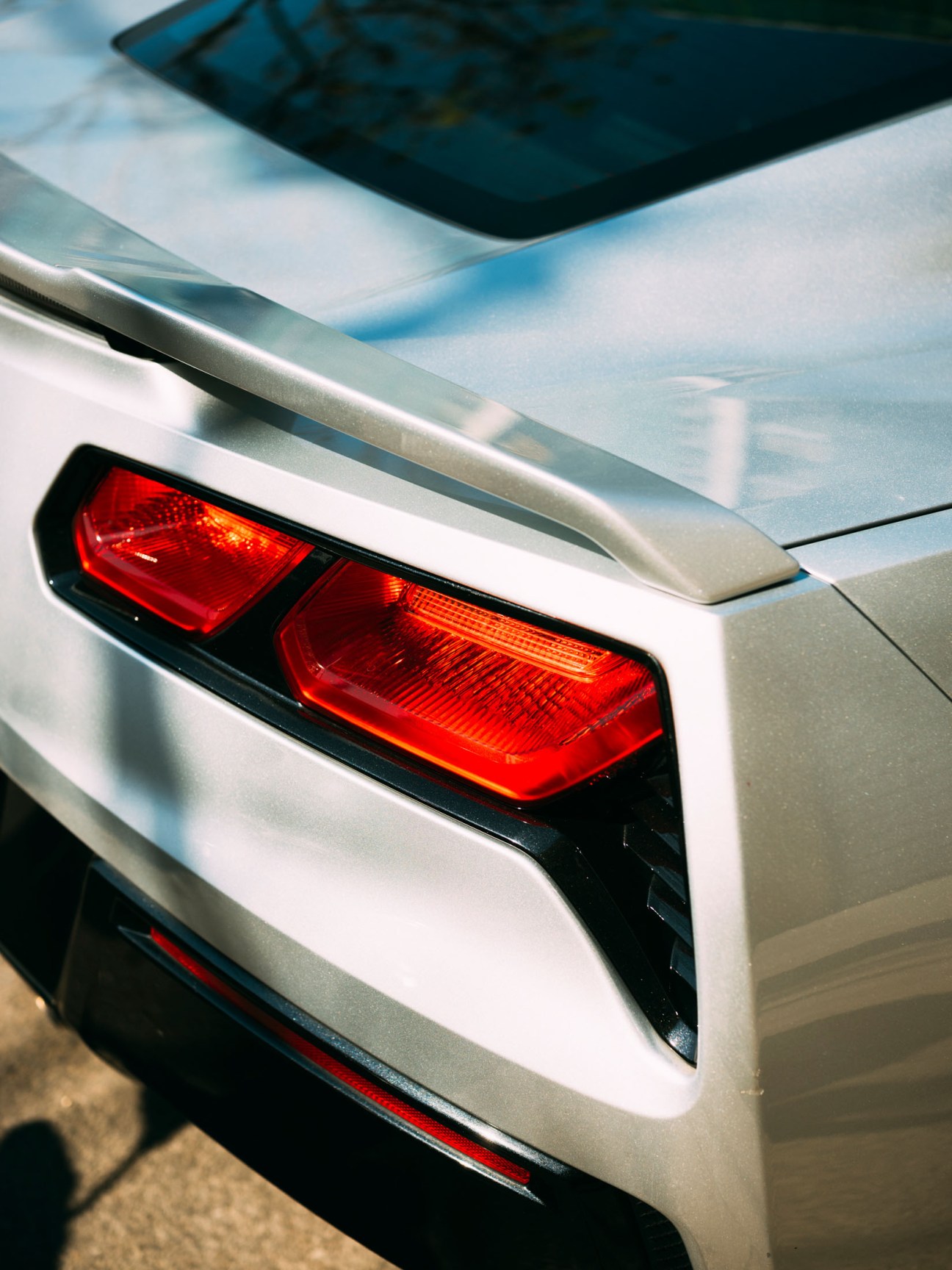 Close-up of a white car's rear taillight and body panel in bright sunlight.