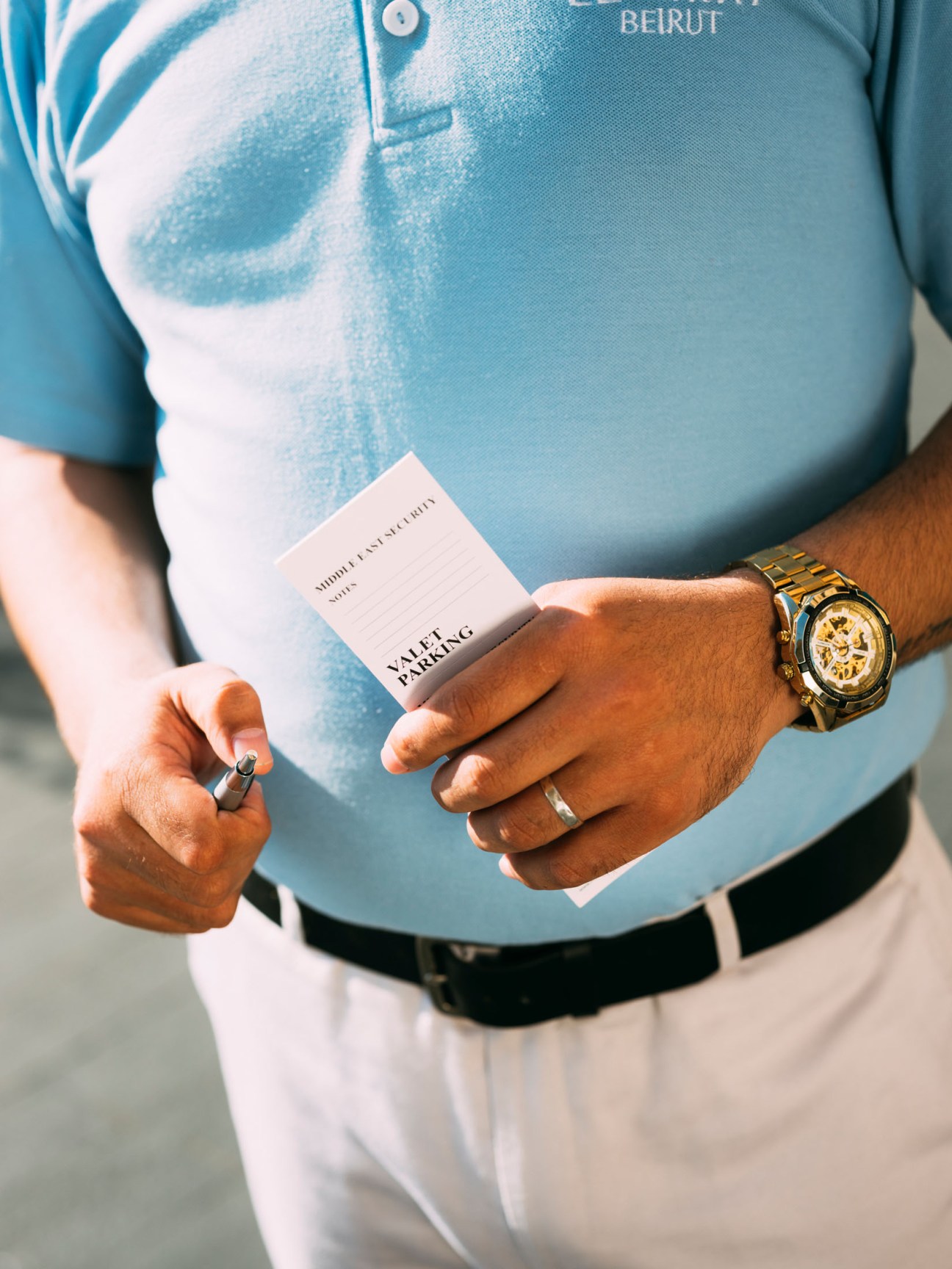 Beirut valet attendant in light blue shirt holding valet parking ticket, displaying luxury watch and rings.