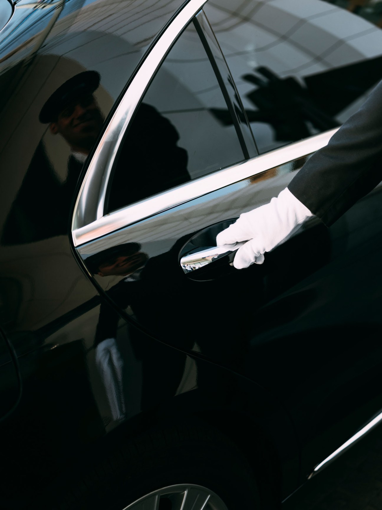 Valet in white gloves and dark suit opening car door handle.