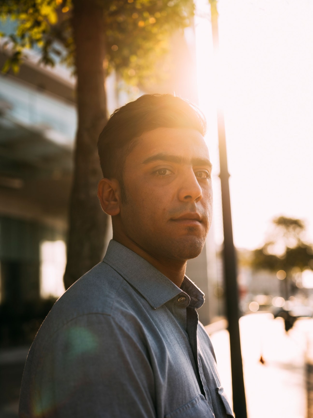 A man in a blue shirt stands on a Beirut street at sunset, backlit by golden hour light.