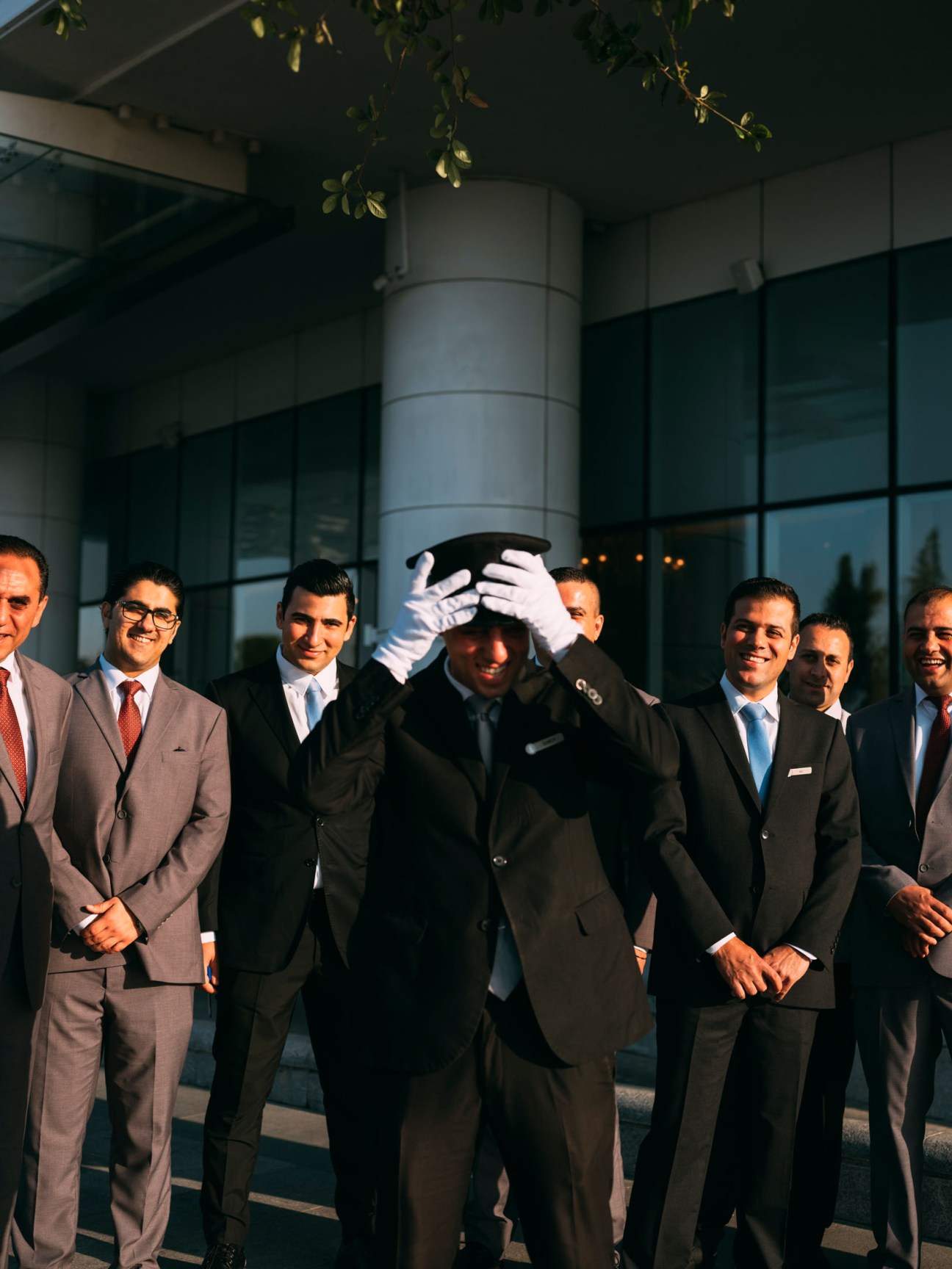 Group of men in business suits standing together, one adjusting a white hat with white gloves.