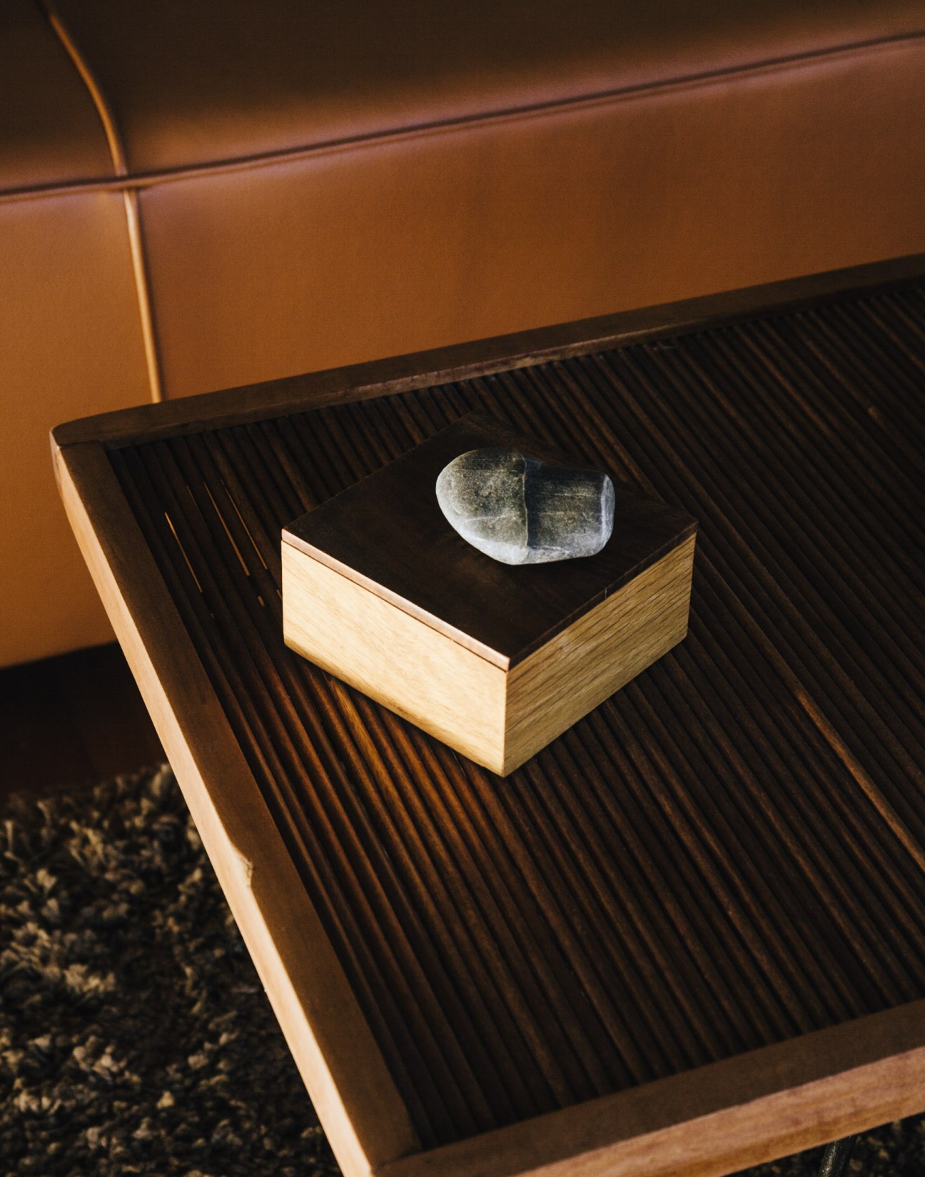 A wooden box with black top displaying a smooth stone object on a striped wooden surface.