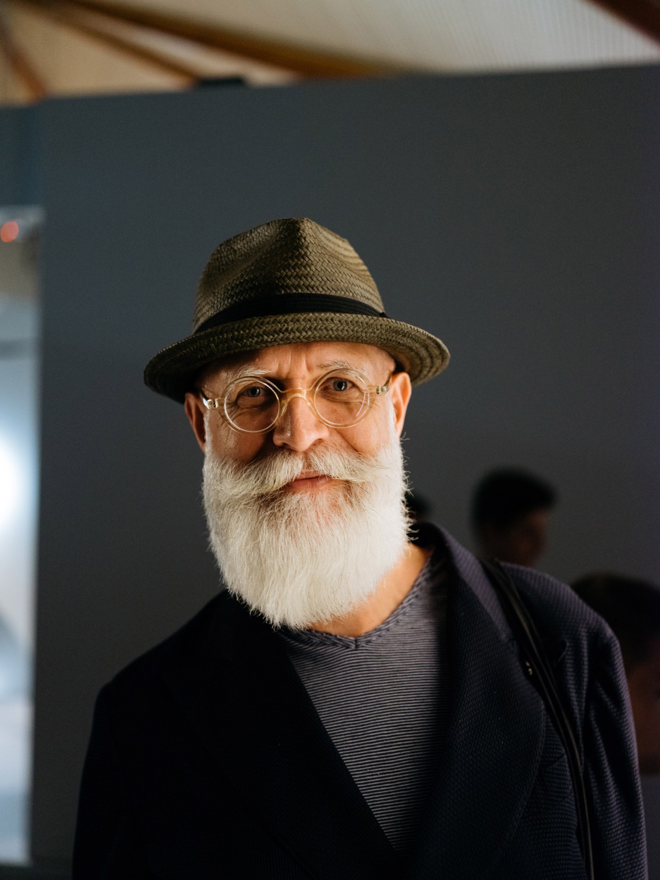 An older man with white beard wearing glasses and a straw hat at the design fair