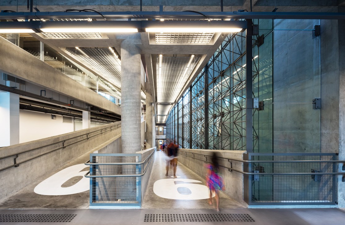 Interior walkway with concrete ramps, metal railings, and glass panels at Sesc 24 de Maio in São Paulo.