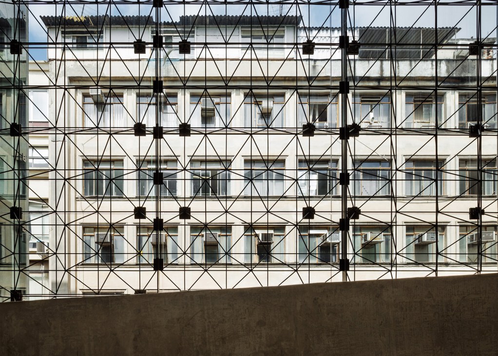 Geometric grid facade of Sesc 24 de Maio with black steel framework overlaying modernist glass and concrete building.