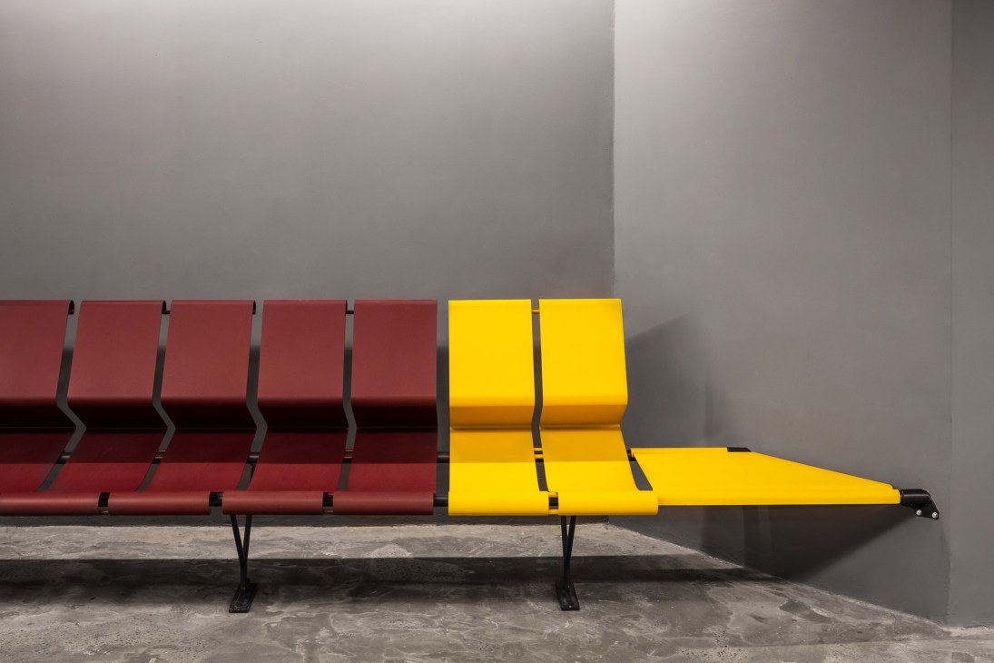 Red and yellow modular seating benches arranged in a theatre foyer against a concrete wall.