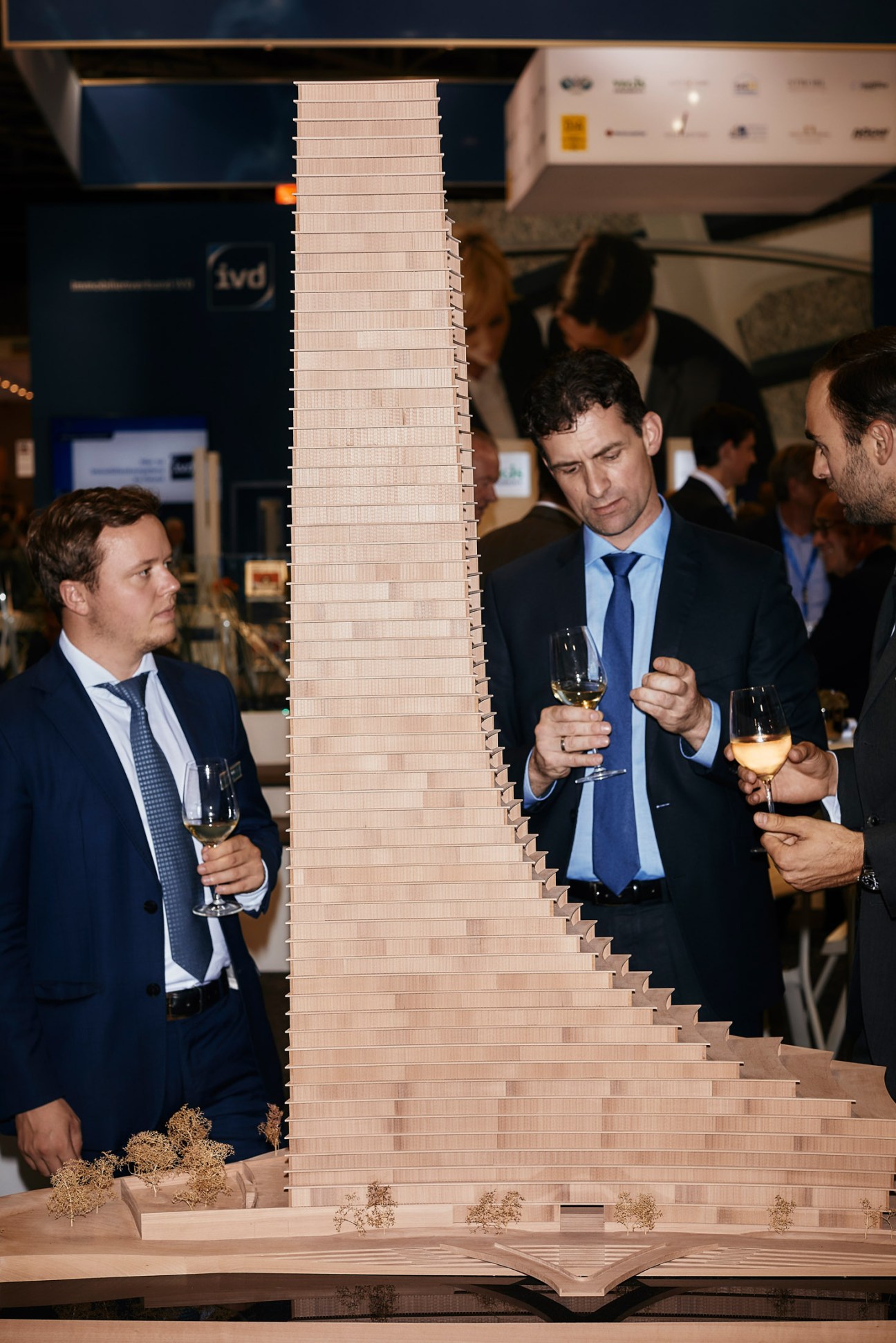 Men in suits examine a tall architectural model of a building at an Expo Real booth.