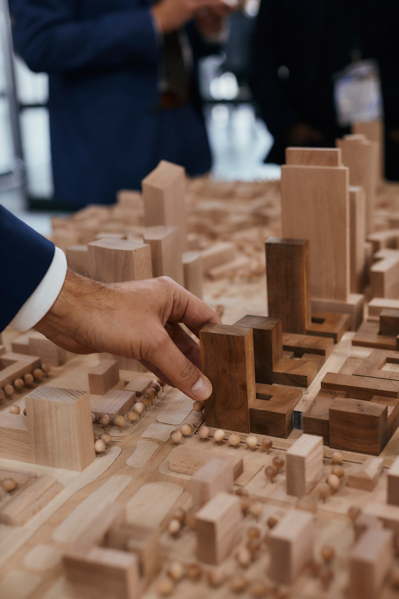 A hand in a navy suit jacket points to a wooden architectural model at Expo Real.