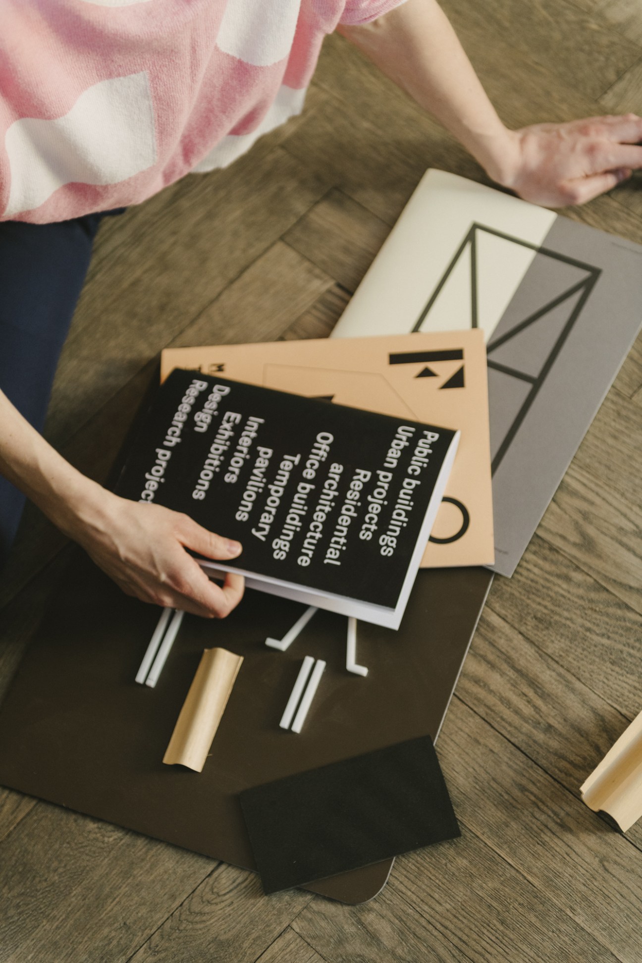 Person in pink and white cardigan browsing through design projects and printed materials on a wooden surface.
