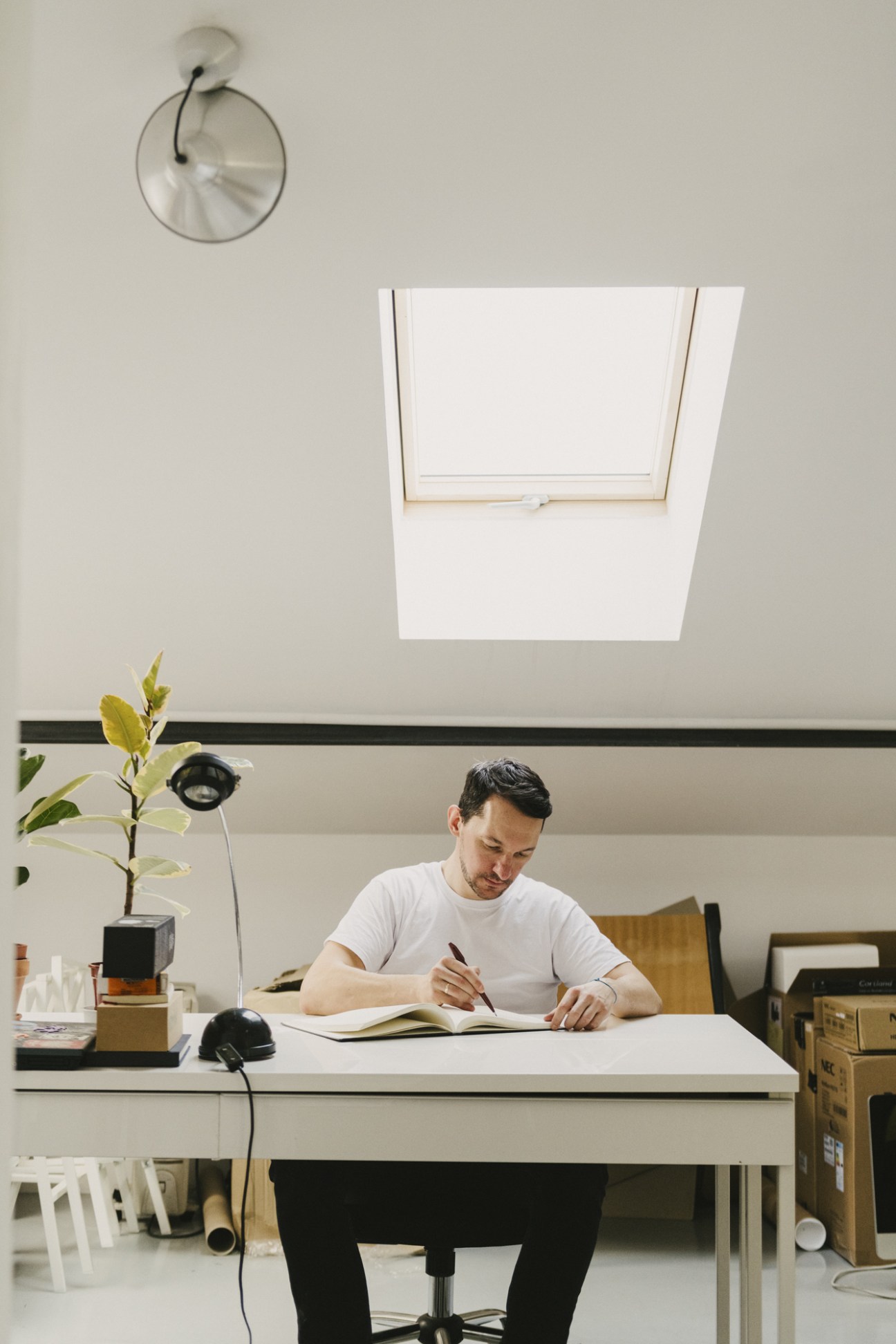 Edgar Bak sitting at a desk in a minimalist studio, sketching in a notebook.