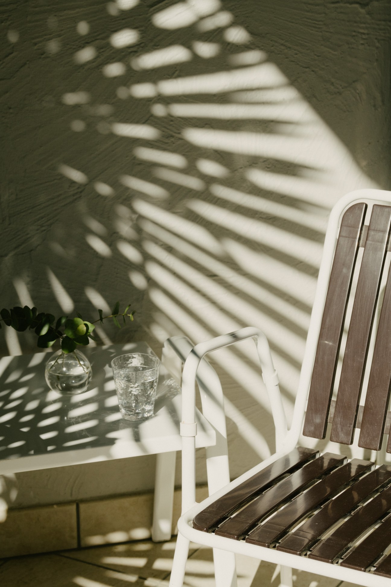 White Manufakt café chair with dark wood slats on a sunlit terrace casting tree shadows.