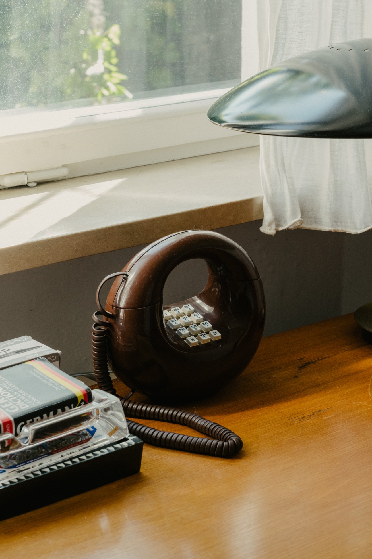 Vintage brown rotary telephone with coiled cord on wooden desk by window