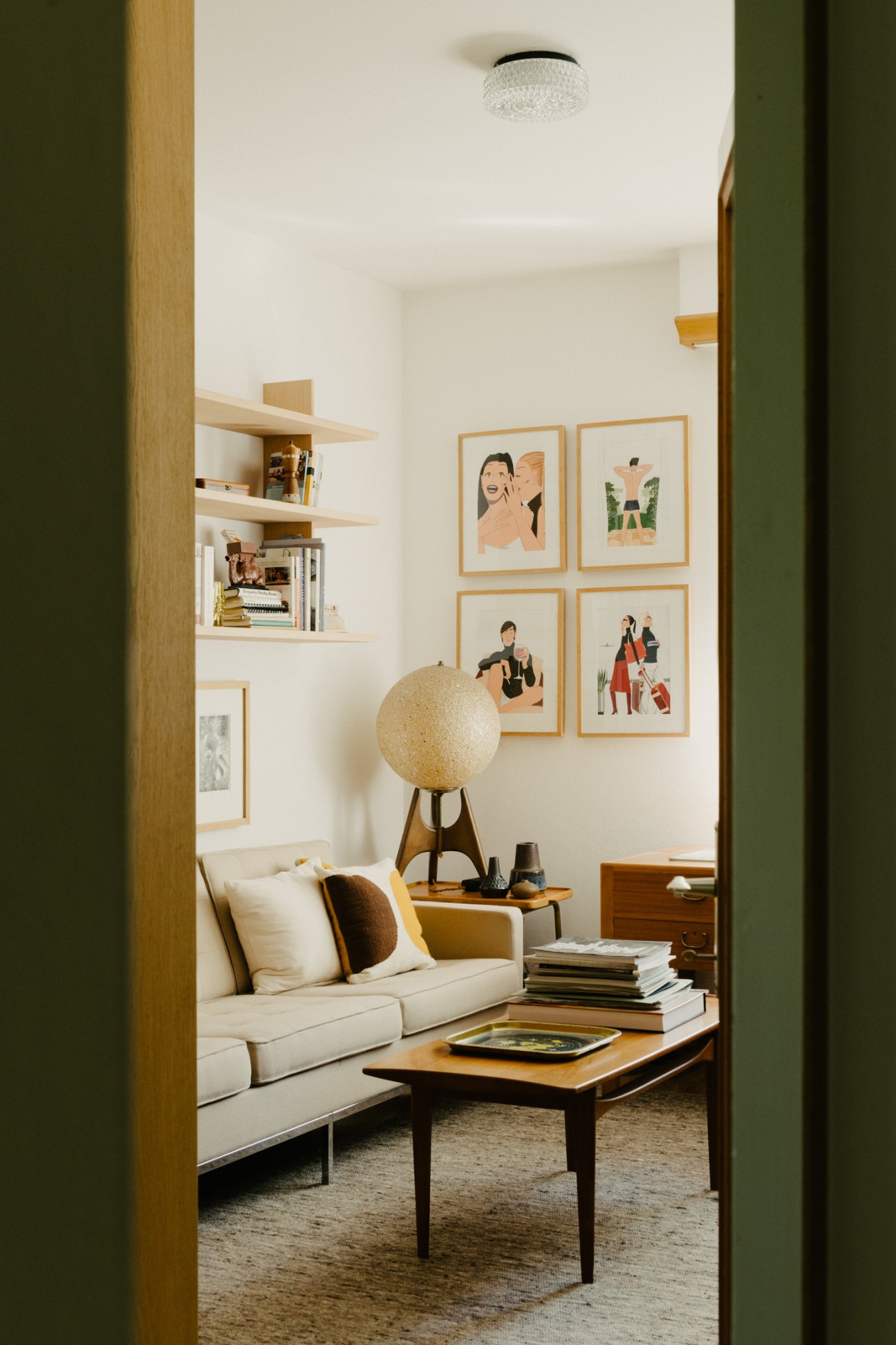 Interior room with cream sofa, wooden coffee table, globe lamp, and framed illustrations by Jordi Labanda on wall.