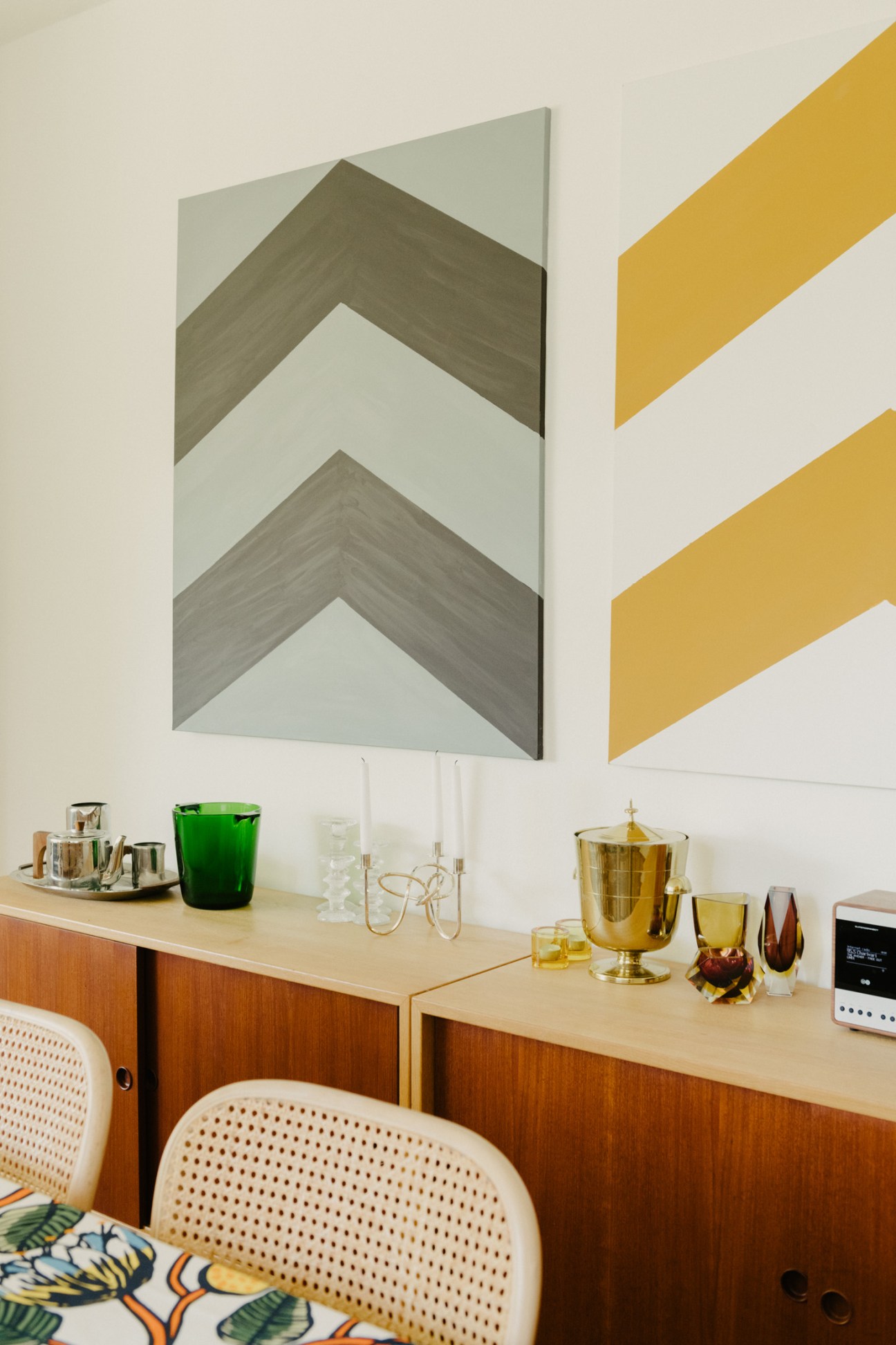 Chevron artwork by Virge displayed on a cream wall above a mid-century modern sideboard with decorative glassware and accessories.