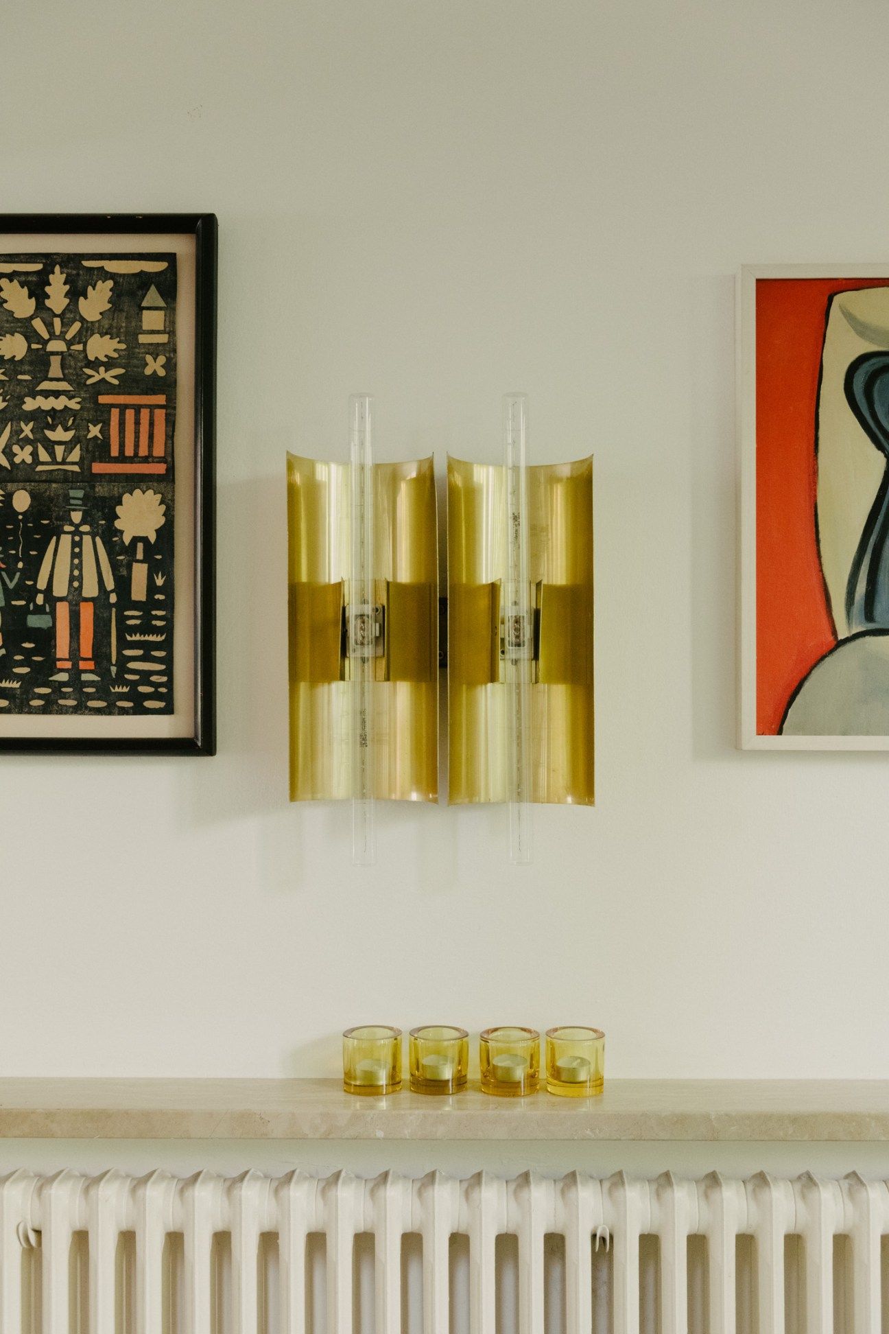 Vintage 1950s Italian cinema lights with brass reflectors and clear glass cylinders displayed on a white wall above four yellow glasses.
