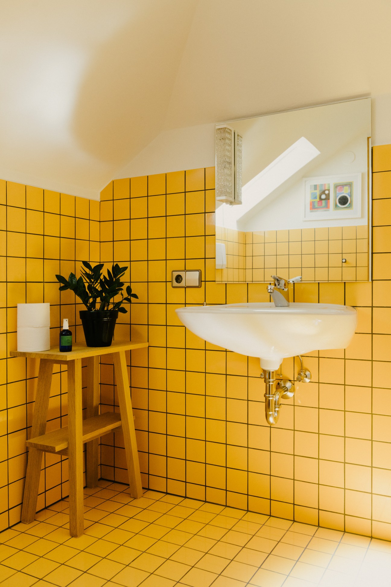 Bright yellow tiled bathroom with white sink, wooden shelf, and skylight