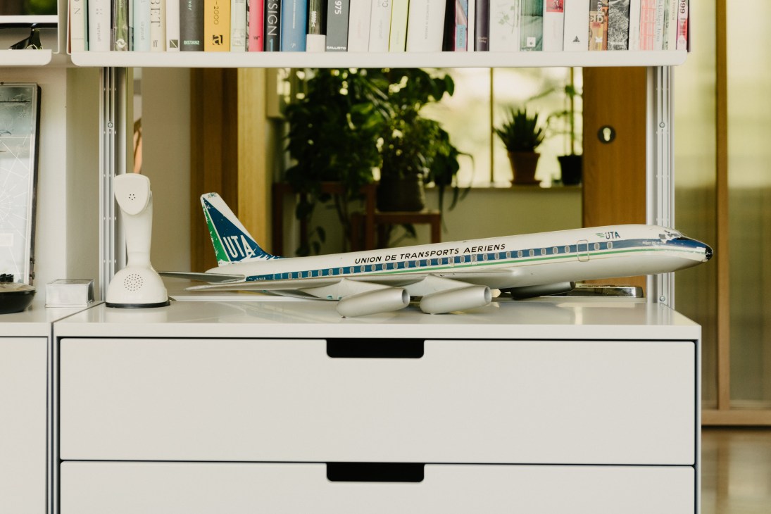 Union de Transports Aériens model airplane displayed on a white Vitsoe 606 shelving unit with books.