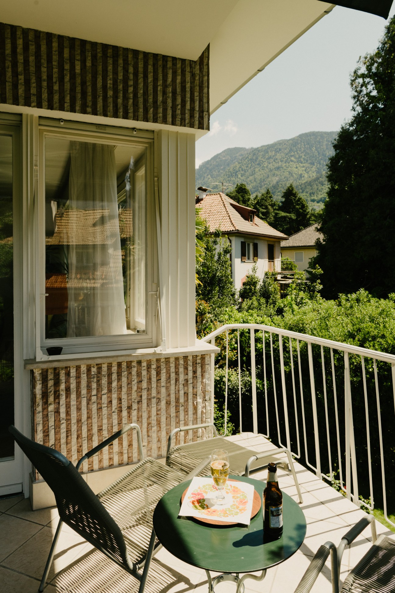 Outdoor balcony with green table, chairs, salad plate and beer overlooking Dolomite mountains.