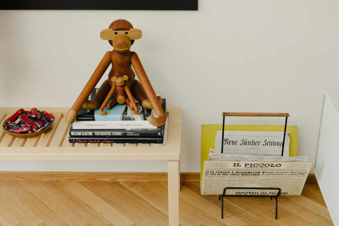 Mid-century modern wooden monkey figurine by Kay Bojesen sitting on books next to a smaller monkey toy and Swiss Army knives in a wooden tray.