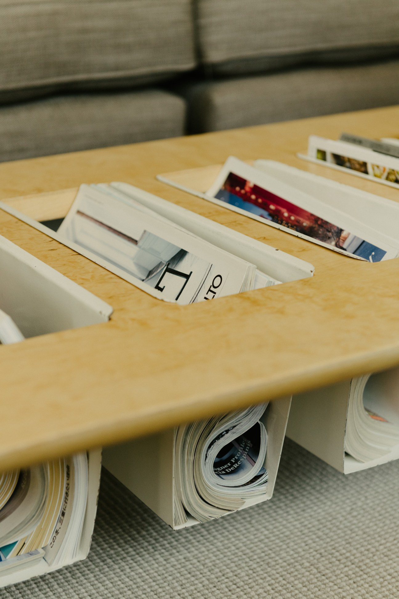 Magazine holder on rare 1970s Bruno Mathsson coffee table with organized publications and gray upholstered seating in background.